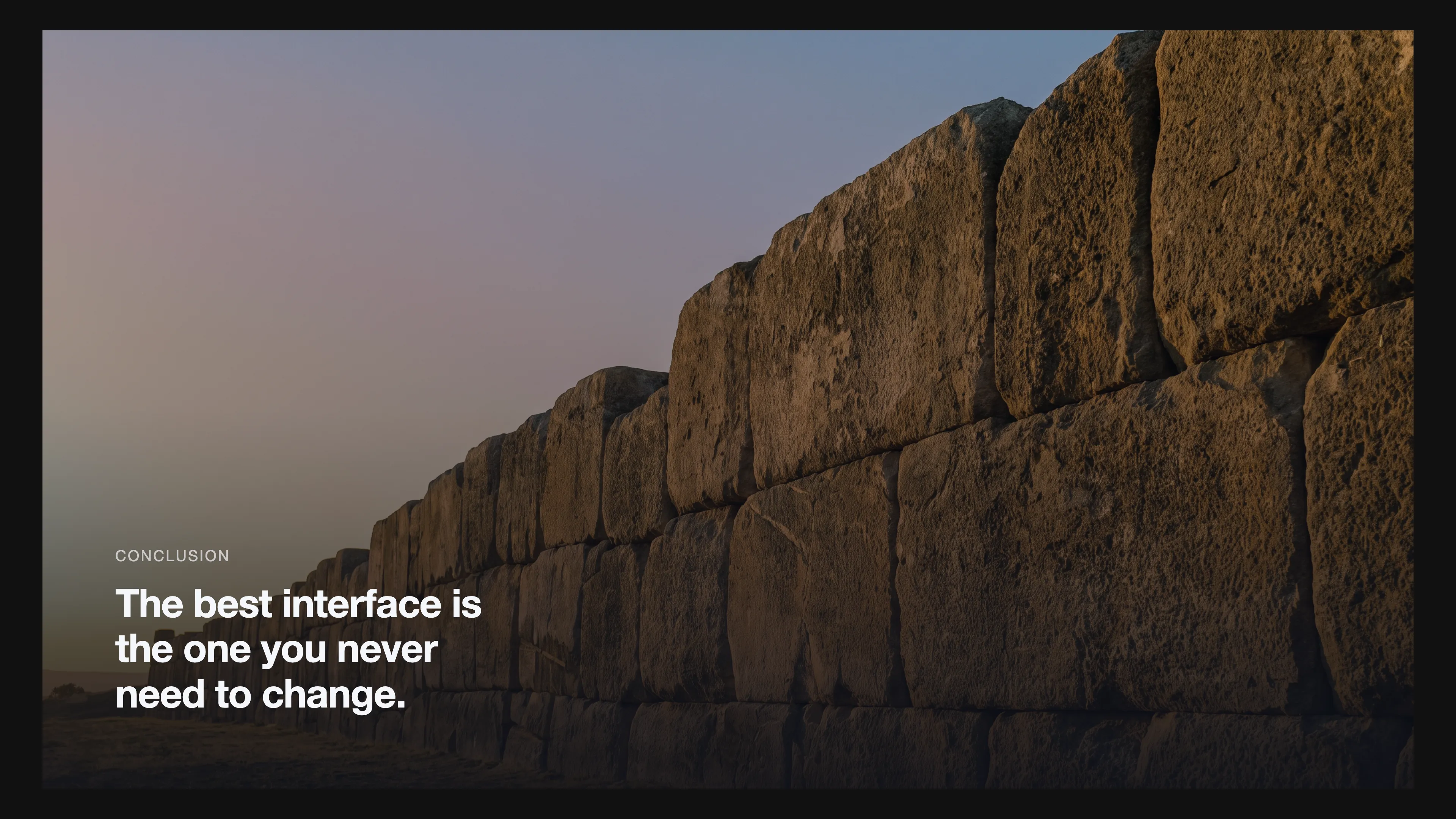 Cinematic scene of a monolith stone wall under calm golden sky, symbolizing an unchanging interface. Overlay text: 'The best interface is the one you never need to change.'